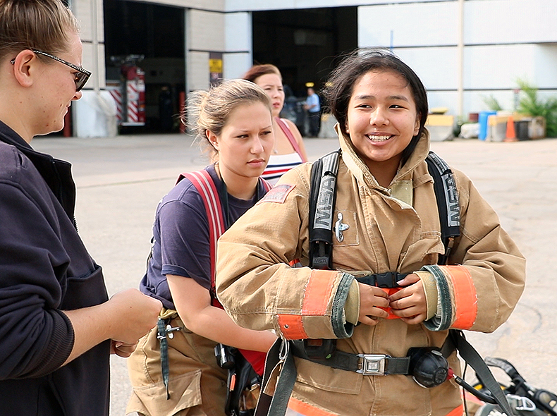 A youth participant being helped into firefighter gear