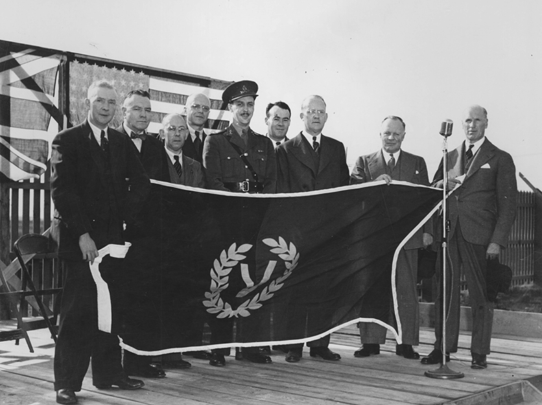 Group of unidentified men and a member of the military holding up a Victory Day flag
