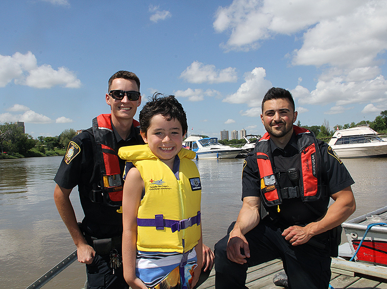 Boy wearing lifejacket standing next to police officers